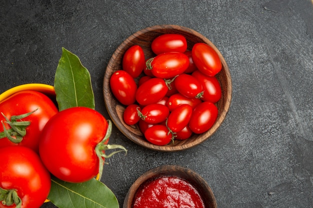 Top close view a bucket with tomatoes bowls with cherry tomatoes and ketchup on dark ground with free space