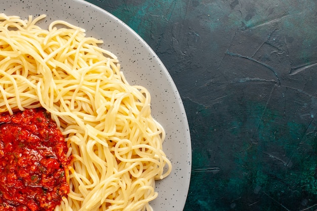 Top close view cooked italian pasta with minced meat and tomato sauce on the dark-blue surface