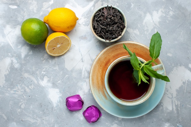 Top close view cup of tea with fresh lemons candies and dried tea on the light table, tea fruit citrus color