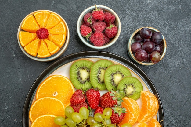 Free photo top close view different fruits composition fresh and sliced fruits on dark background health ripe fresh fruit mellow