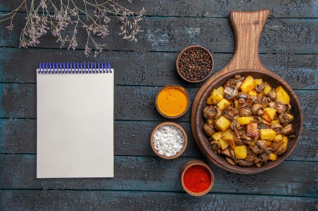 Free Photo top close view dish and spices a dish of potatoes and mushrooms on the cutting board and colorful spices around it next to the notebook and branches