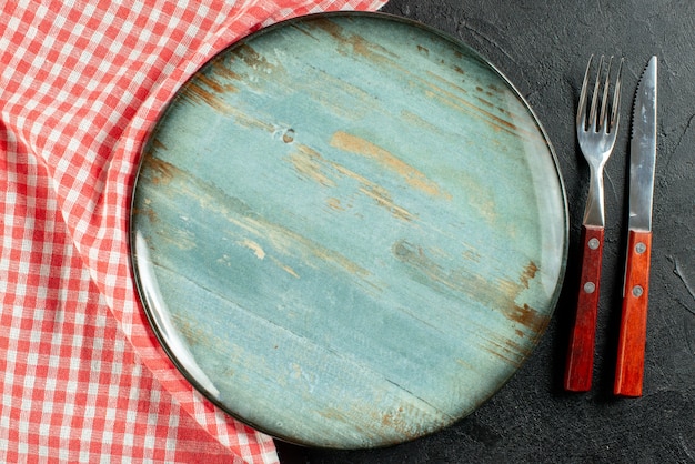 Free photo top close view fork and knife red white checkered napkin round plate on dark table