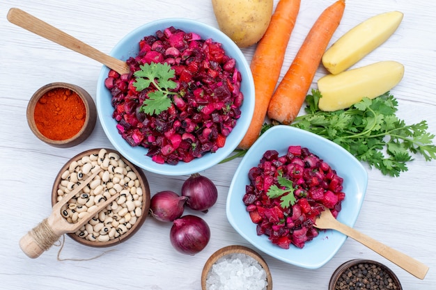 Top close view of fresh beet salad with sliced vegetables inside blue plates with ingredients on light desk, vegetable salad food meal health snack