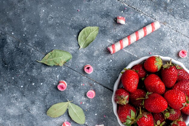 Free photo top close view of fresh red strawberries inside plate along with stick candies on grey , fruit berry fresh candy mellow sweet