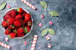 Free photo top close view of fresh red strawberries inside plate along with stick candies on grey , fruit berry fresh candy sweet