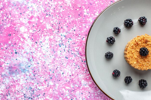 Top close view of little cake with berries on pink surface