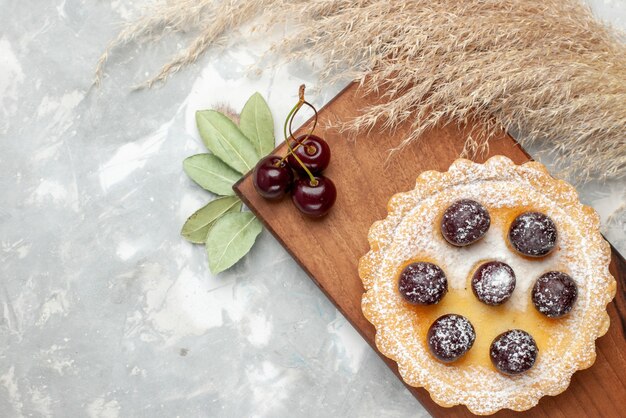 Top close view of little cake with sugar powder fruits on light, cake cream fruit sweet