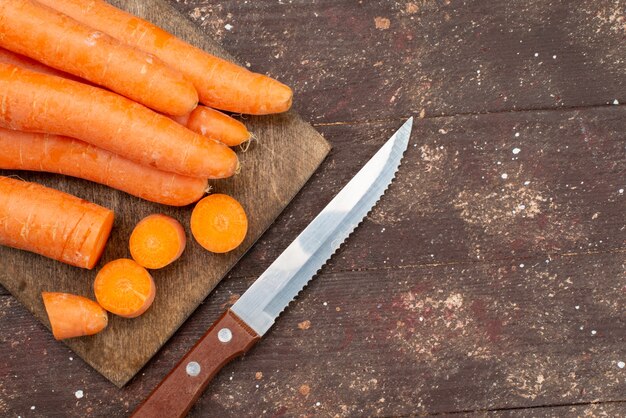 Top close view orange carrots sliced and whole on brown