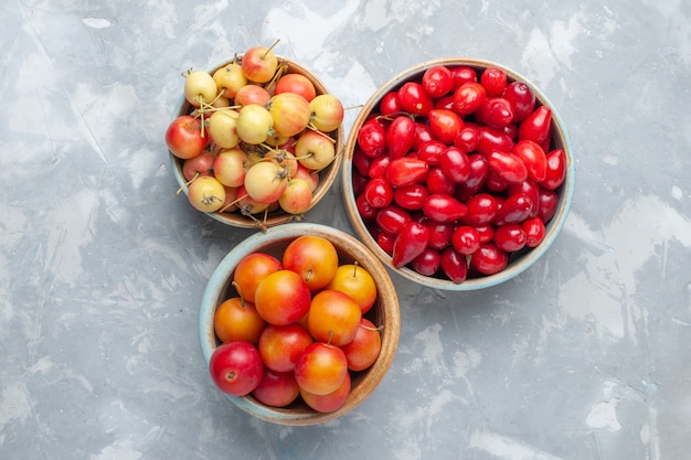 Top close view red dogwoods with cherry-plums and cherries on the white desk fruit fresh mellow juice vitamine