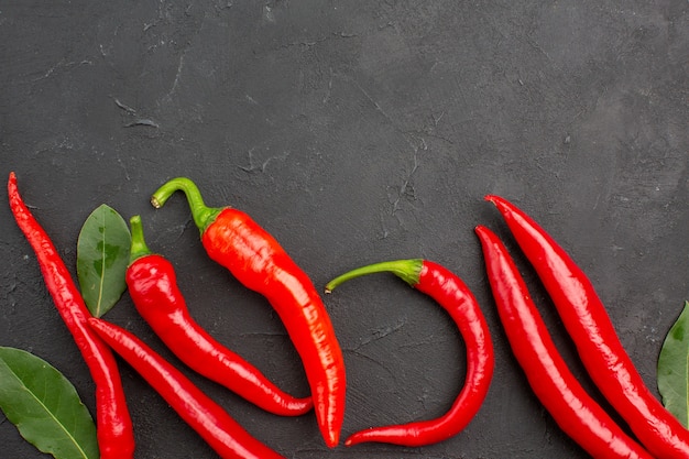 Top close view red peppers and pay leaves on black table with copy space