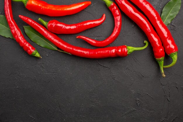 Top close view red peppers and pay leaves at the top of black table with free space