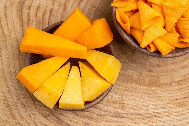 Top close view slices of cheese and chips in bowls on wooden table