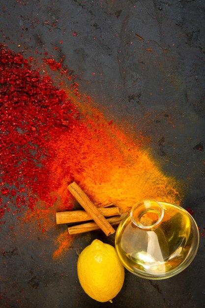 top  colorful spices with a bottle of olive oil cinnamon sticks and lemon on black