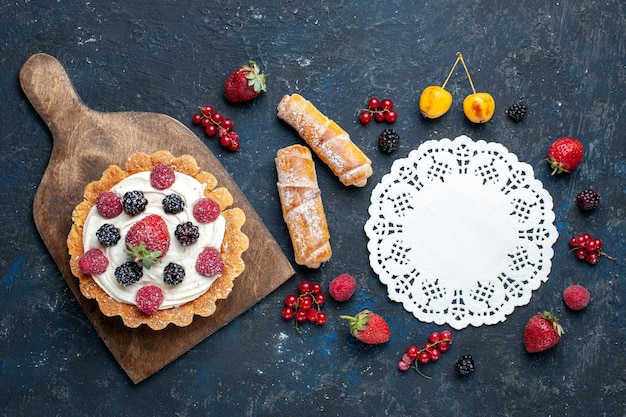 Top distant view delicious little cake with cream and berries along with bangles on dark desk, berry fruit biscuit