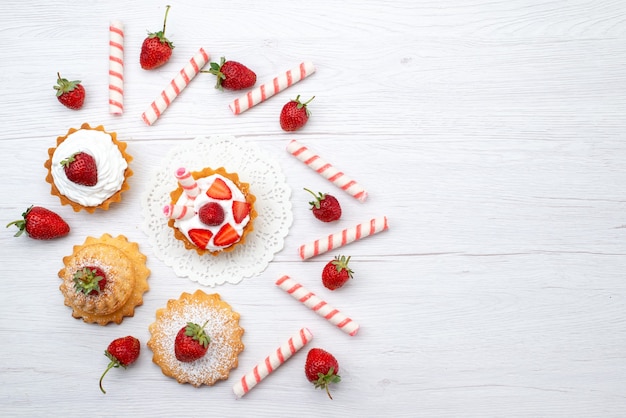 Top distant view of little cake with cream and sliced strawberries candies on white desk, fruit cake berry sweet sugar bake