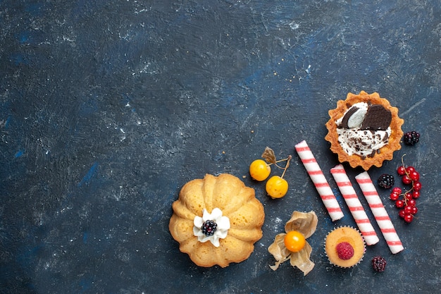 Free photo top distant view of little delicious cake along with cookie and pink stick candies fruits on dark desk, biscuit cake fruit