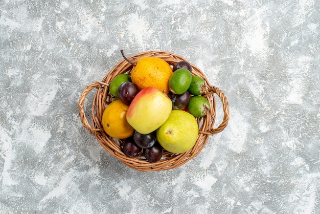 Top distant view plastic wicker basket with apple pears feykhoas plums and persimmon at the center of the grey table