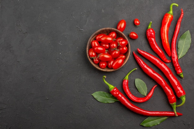 Top distant view red peppers and pay leaves and a bowl of cherry tomatoes on black table