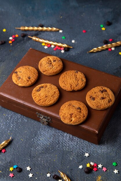 Top distant view yummy chocolate cookies on the brown case with colored little star signs and candles on the dark-grey background cookie biscuit sweet tea