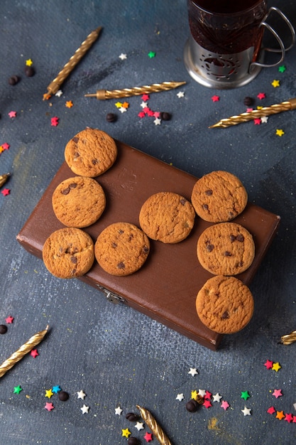 Top distant view yummy chocolate cookies on the brown case with tea and candles on the dark-grey background cookie biscuit sweet