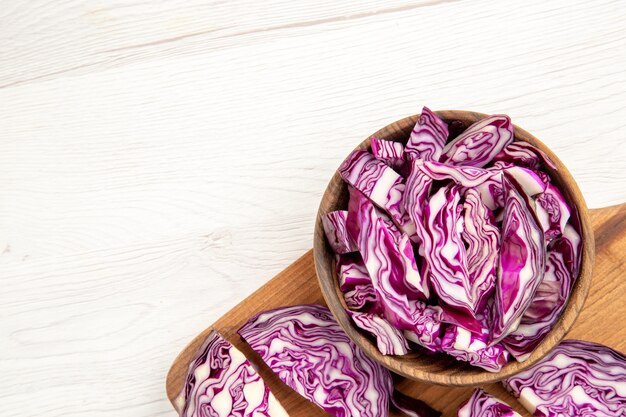 Top half view chopped red cabbages in wooden bowl on cutting board on white surface with free space