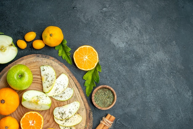 Free photo top half view cut apples and mandarines on rustic serving board cinnamon dried mint powder bowl cumcuat on dark table with copy place