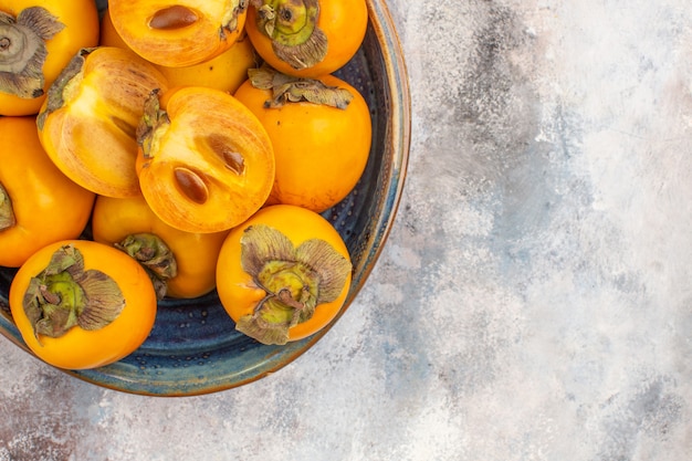 Free Photo top half view delicious persimmons in round wood box on nude background