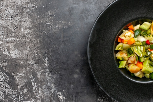 Top half view green tomato salad on black oval plate on dark background