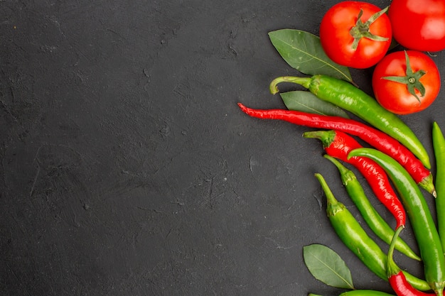 Top half view hot red and green peppers and tomatoes bay leaves at the right side of black ground