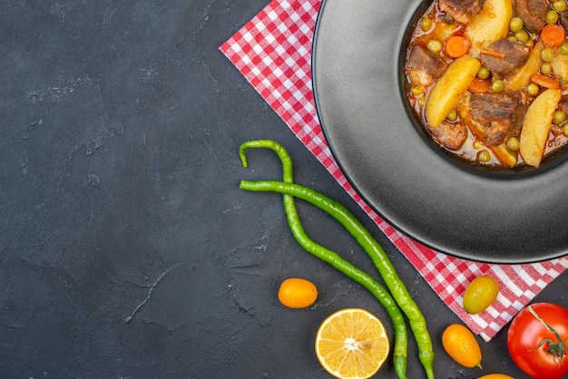 Top half view meat soup with garniture on round plate fresh vegetables on black table