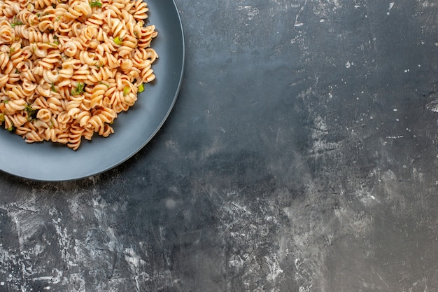 Top half view rotini pasta on round plate on dark surface free space food photo