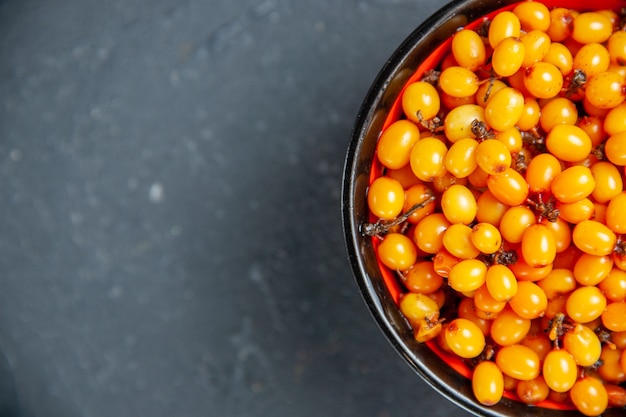 Top half view sea buckthorn in bowl on dark red surface free space