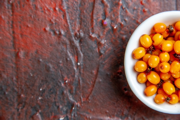 Free Photo top half view sea buckthorn in white bowl on dark red table with copy space