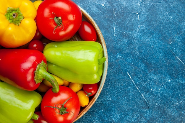 Free photo top half view vegetables cherry tomatoes different colors bell peppers tomatoes on wooden platter on blue table copy place