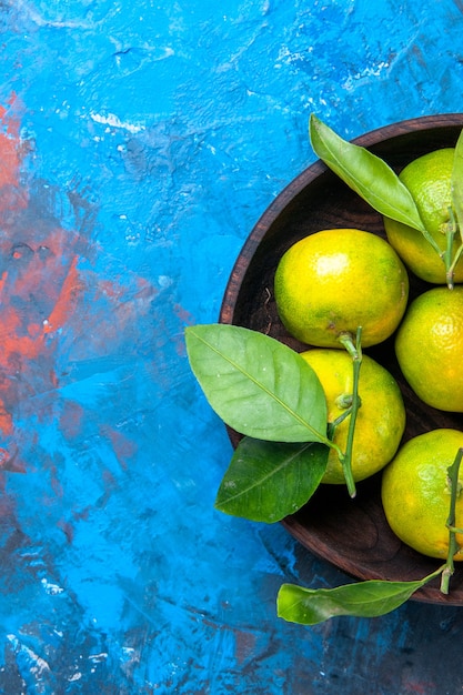 Free photo top half view yellow tangerines with leaves in wooden bowl on blue isolated background free space