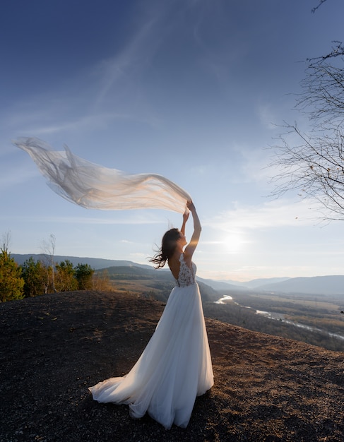 On the top of a hill in the evening, back view of a bride with wavy veil