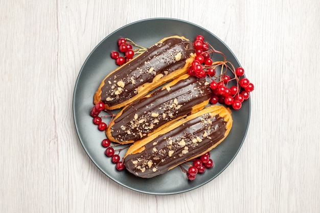 Free photo top left side view chocolate eclairs and currants on the grey plate on the white wooden ground pace