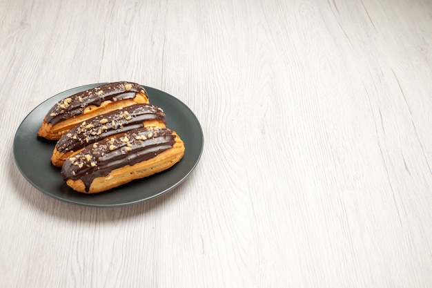 Top left side view chocolate eclairs on the grey plate on the white wooden ground