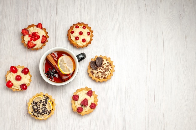 Top left side view lemon cinnamon tea rounded with tarts on the white wooden table