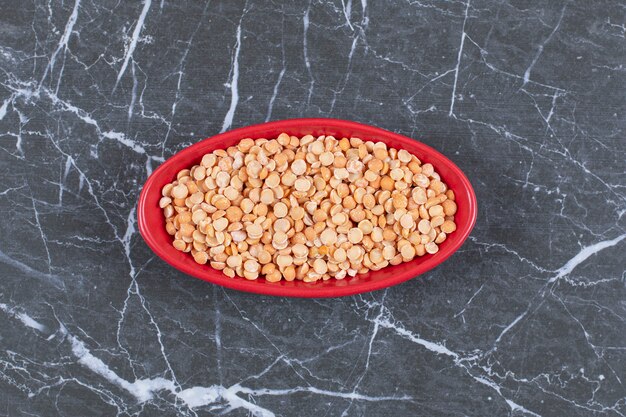 Top up view of dry peas in red bowl over black stone.