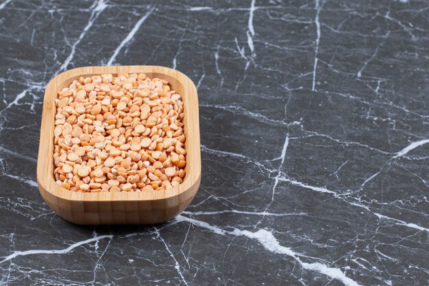 Top up view of dry peas in wooden bowl over black stone.