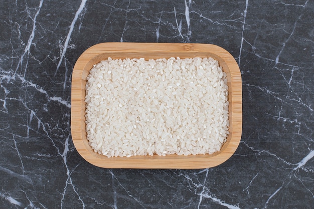 Free photo top up view of wooden bowl full with raw rice on grey black stone.