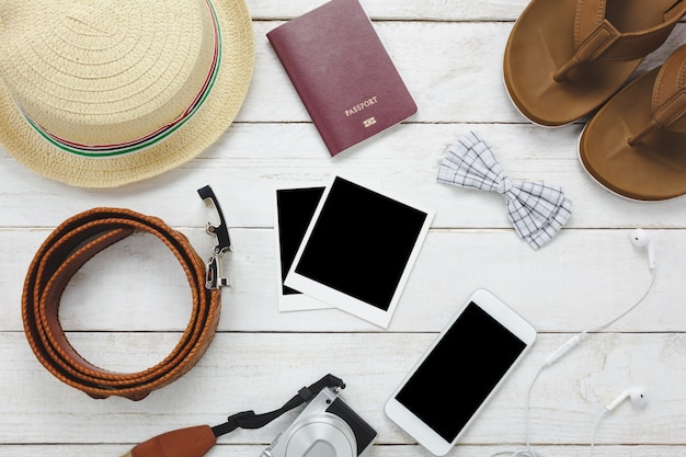 Top view accessoires to travel concept.White mobile phone,hat,passport,camera,photo,sandal on wood table.