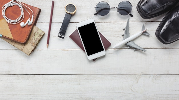 Top view accessoires to travel concept.White mobile  phone and headphone on wooden background.airplane,map,passport,watch on wood table.