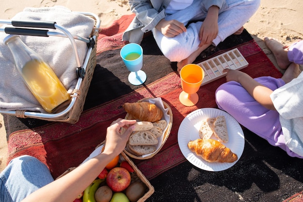 Free photo top view of african american family on picnic on beach. mother and children in casual clothes sitting on blanket, eating bread, drinking juice. family, relaxation, nature concept