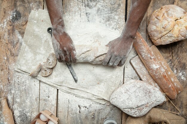 Top view of african-american man cooks fresh cereal, bread, bran on wooden table. Tasty eating, nutrition, craft product. Gluten-free food, healthy lifestyle, organic and safe manufacture. Handmade.