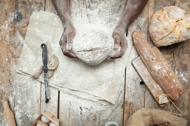 Free photo top view of african-american man cooks fresh cereal, bread, bran on wooden table. tasty eating, nutrition, craft product