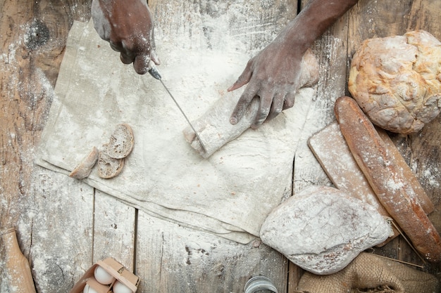 Top view of african-american man cooks fresh cereal, bread, bran on wooden table. Tasty eating, nutrition, craft product