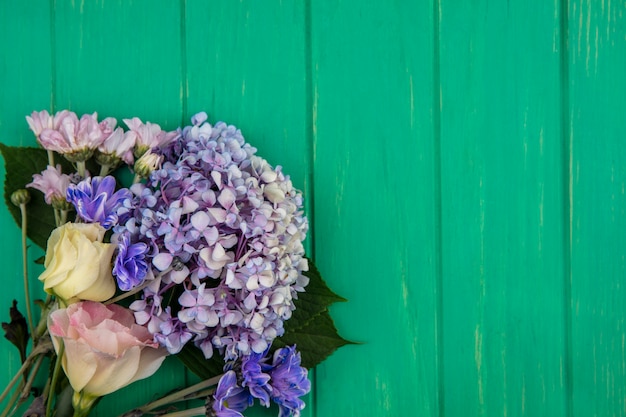 Free photo top view of amazing colorful flowers like gardenzia daisy rose on a green wooden background with copy space