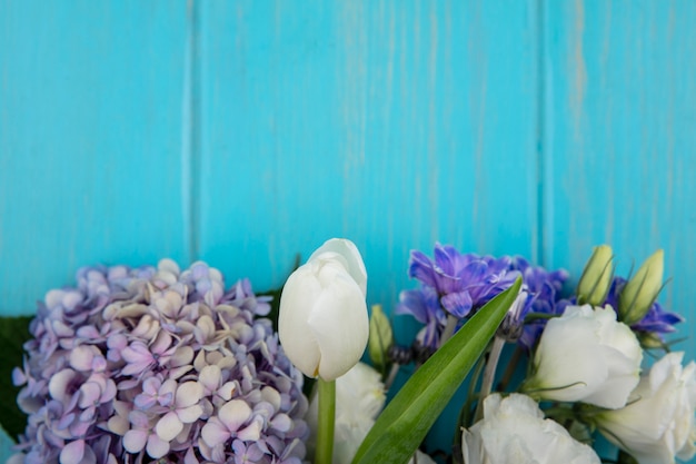 Top view of amazing colorful flowers like lilac rose tulip with leaves on a blue background with copy space